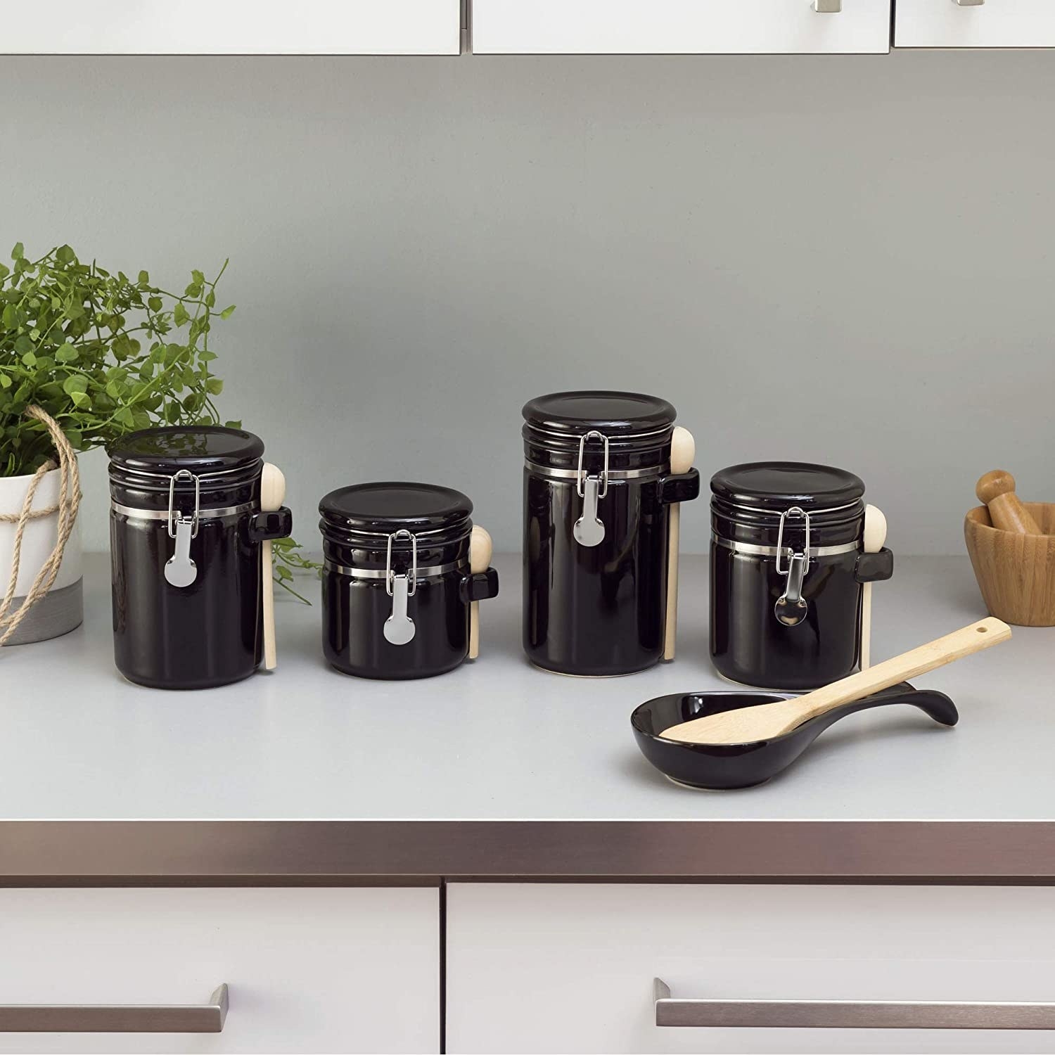 Four canisters and a spoon rest in black ceramic with metal details and wooden spoons on the sides 