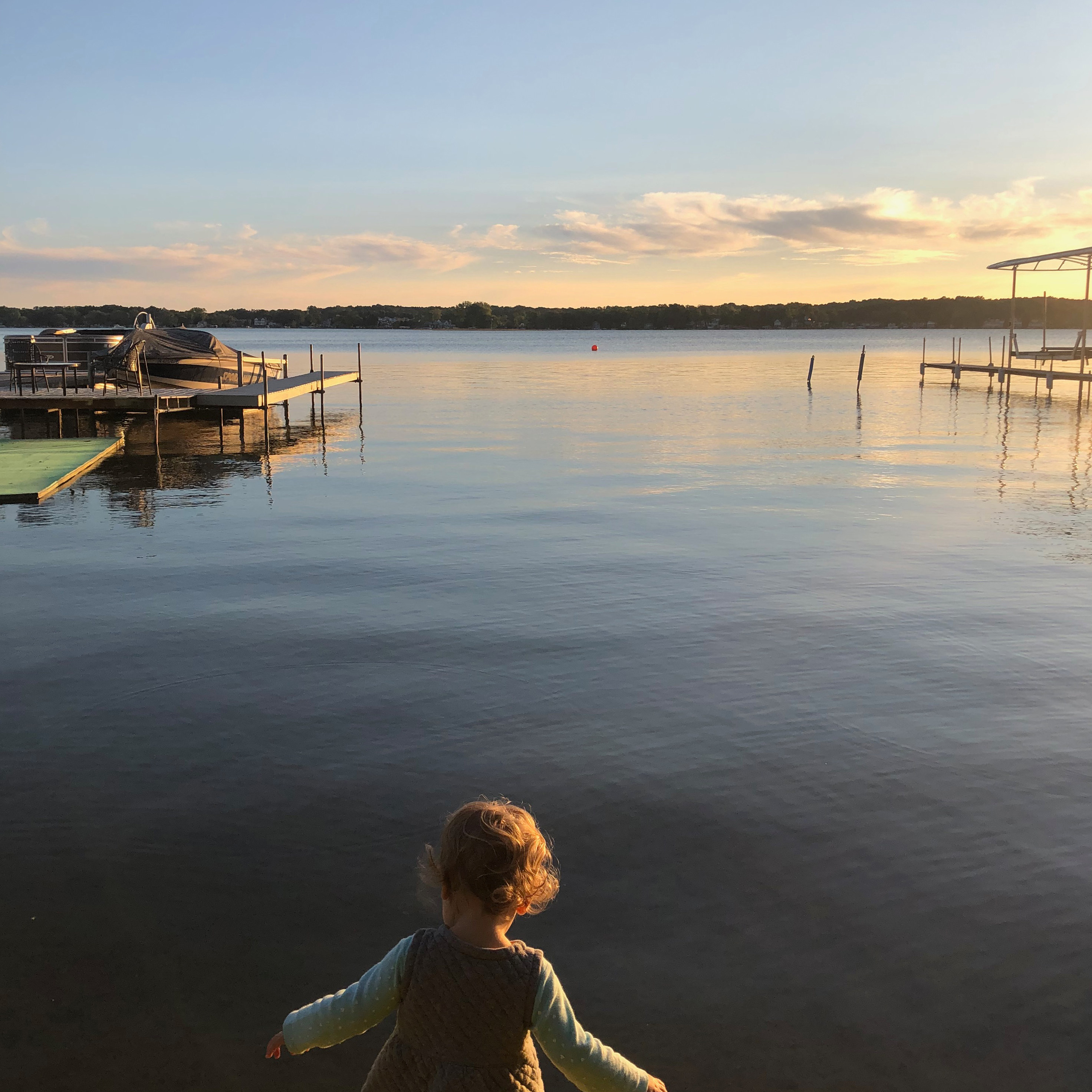 A toddler at the edge of a lake at sunset