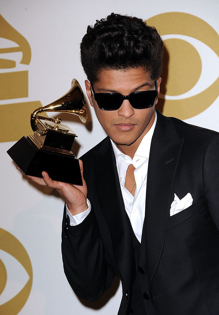 Bruno wearing dark sunglasses and holding up his Grammy to his ear