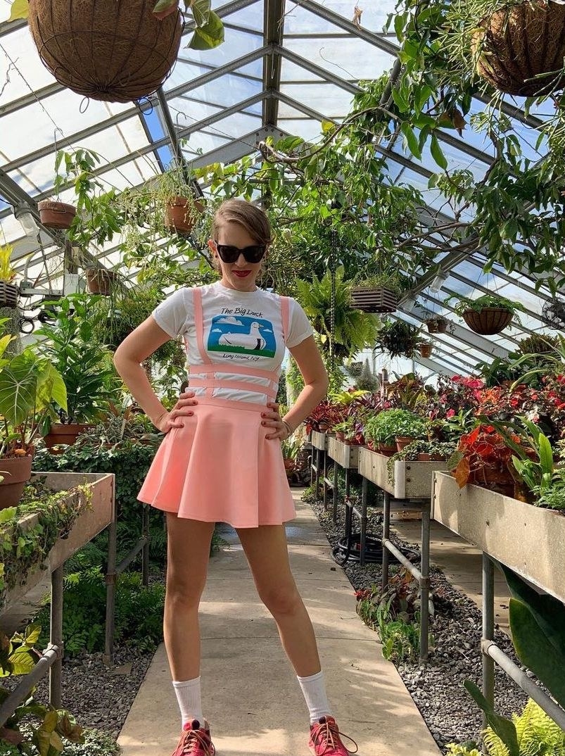a person wearing the pink pinafore with a white graphic shirt inside of a greenhouse