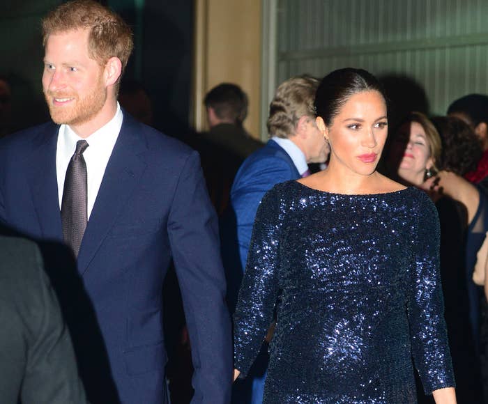 Meghan Markle walking in a concert hall while wearing a sparkling blue dress and holding Prince Harry&#x27;s hand.