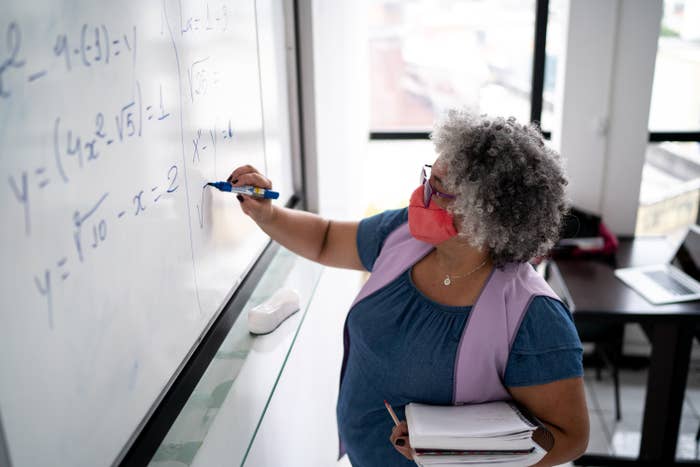 A professor wearing a face mask and writing math equations on a board