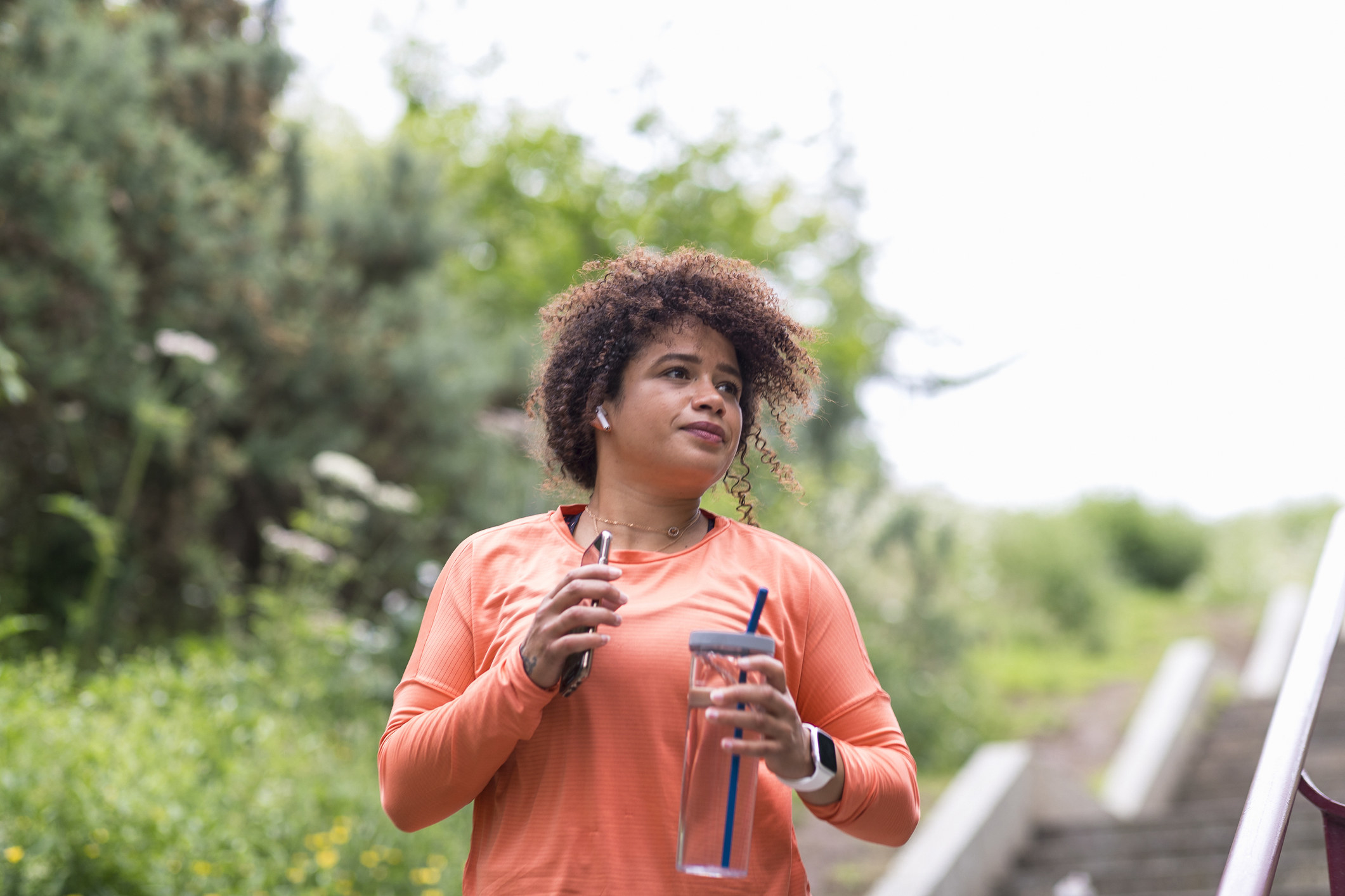 A woman holding a water bottle and her phone as she walks outdoors