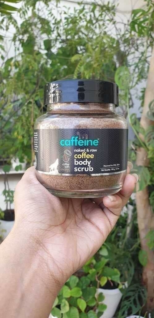 A hand holding the jar of the coffee body scrub.
