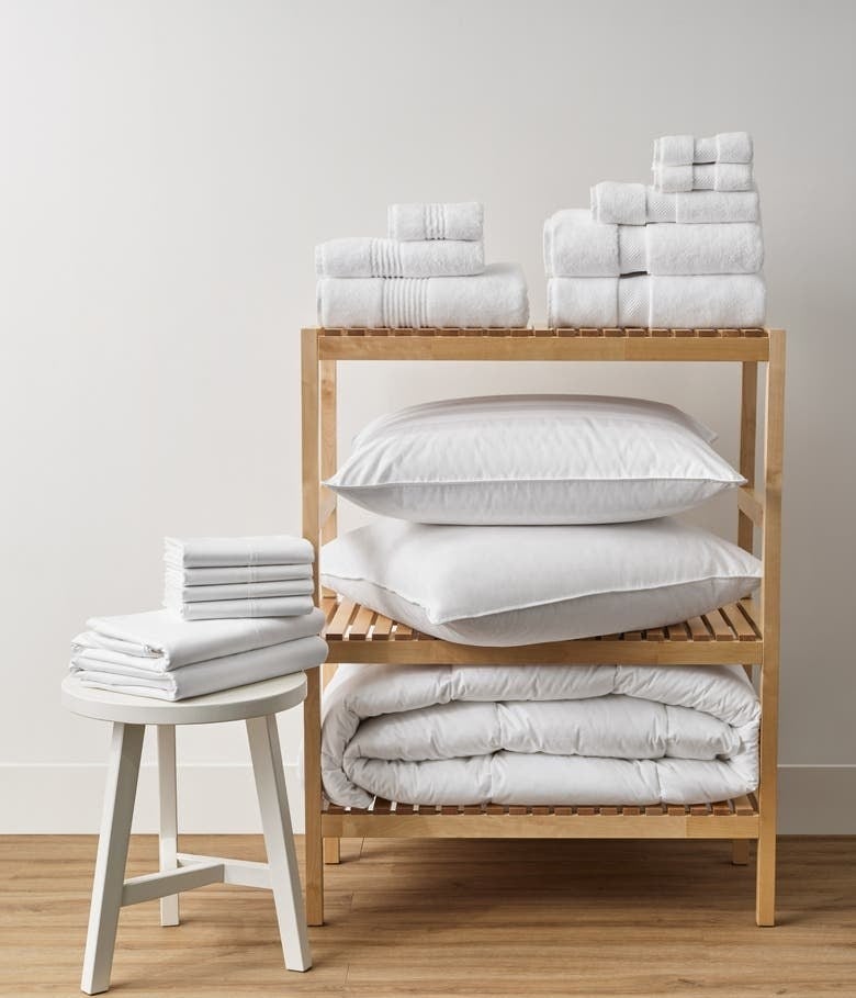 White towels with sheets, pillows and a comforter on a light wood stand