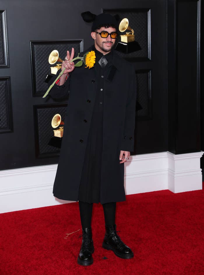 Bad Bunny walks the red carpet in an all-black look at the 2021 Grammys while holding a sunflower