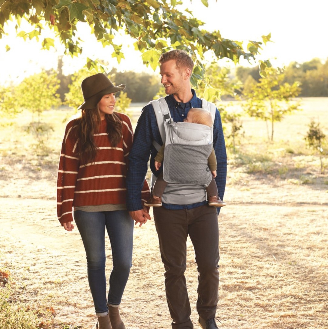 Two people walking with a baby carrier on one of their chests