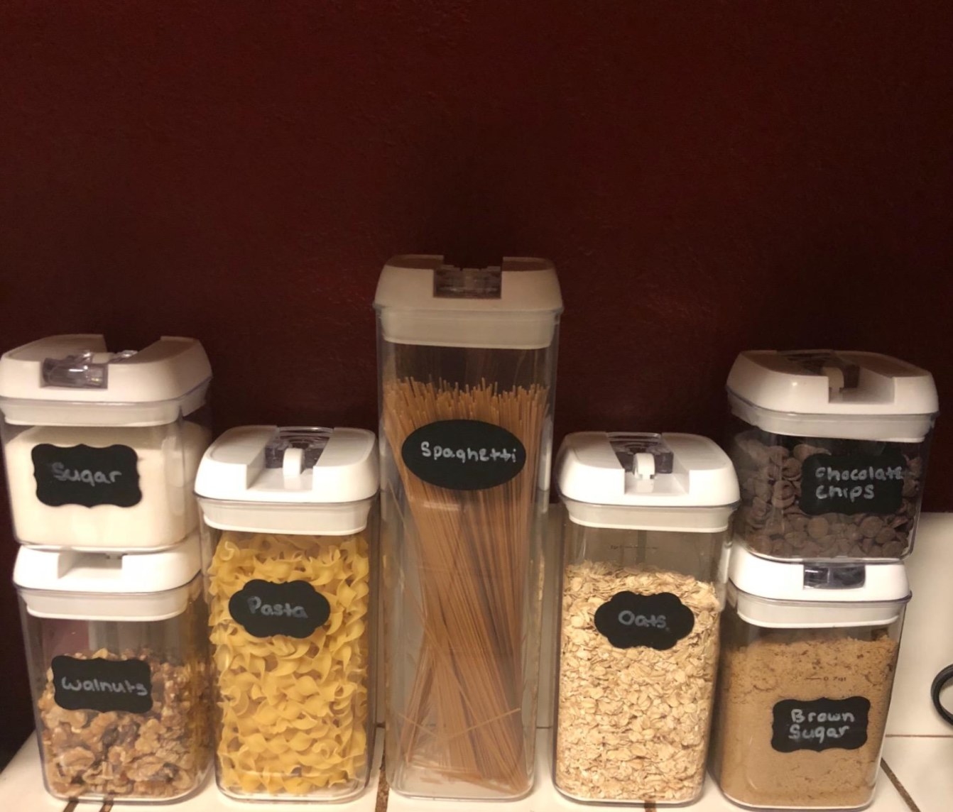 reviewer&#x27;s seven-piece storage container set in a cabinet holding pasta, oats, and sugar