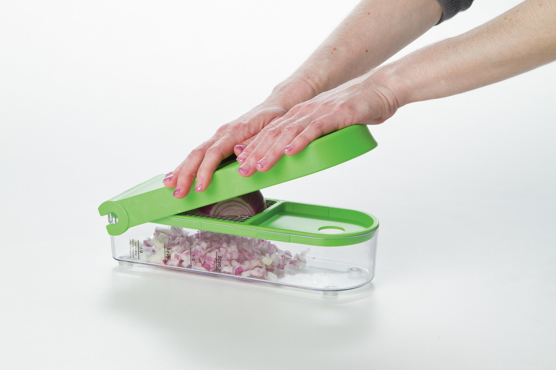 hands using an onion dicer with a green lid to chop an onion