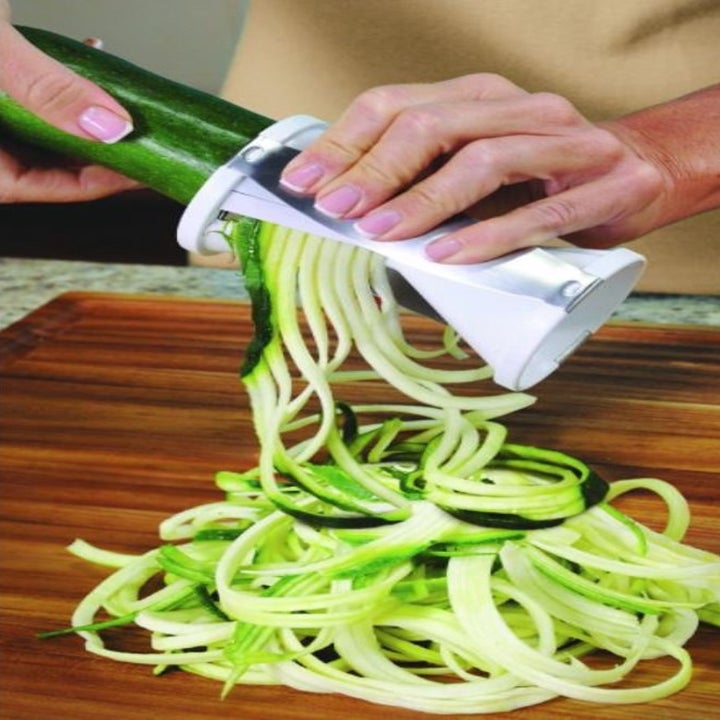 hands using a spiral vegetable cutter to slice zucchini 