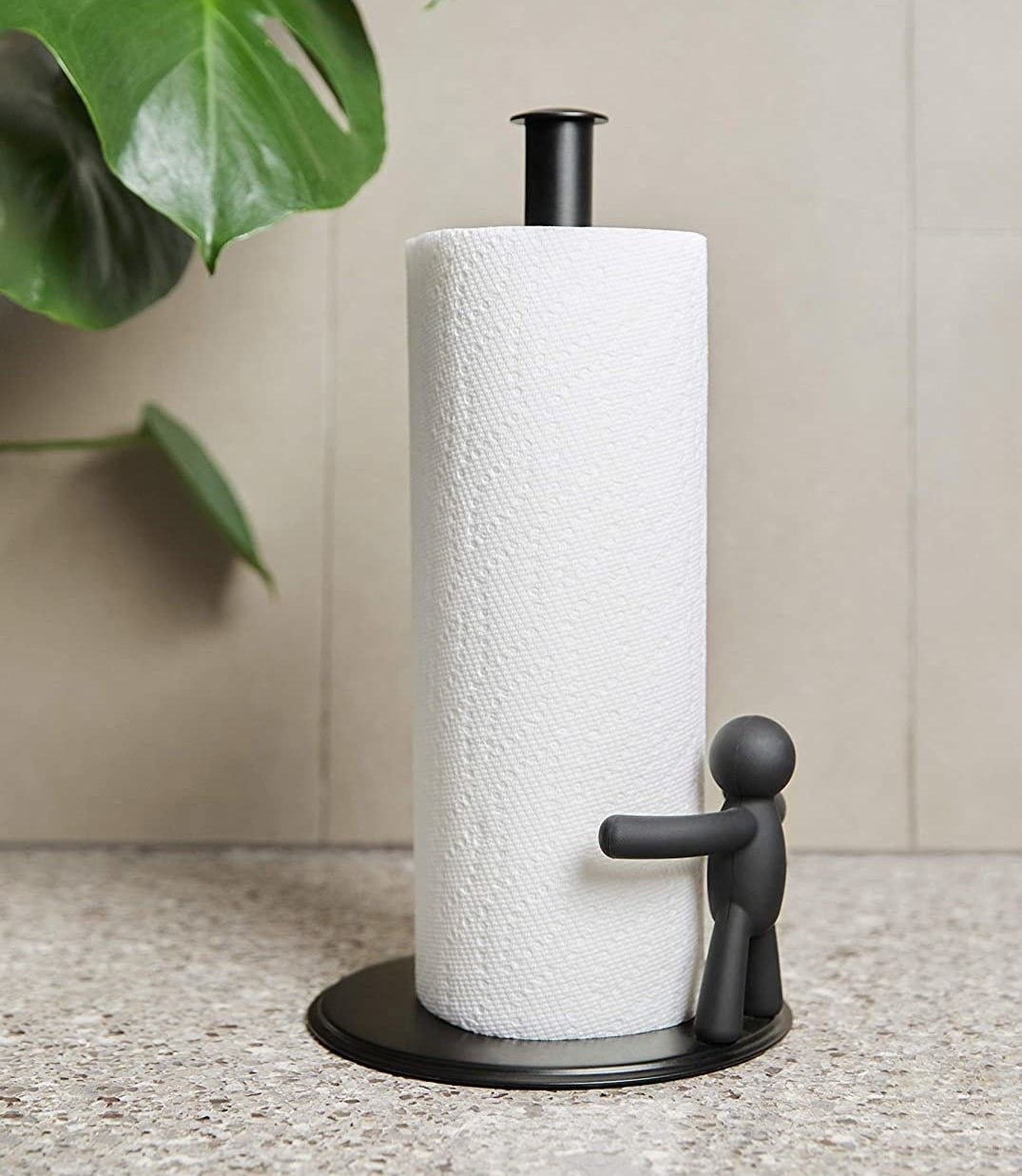 A paper towel roll on a paper towel holder that has a little person on one side with its arms stretched around it like it&#x27;s giving it a hug 