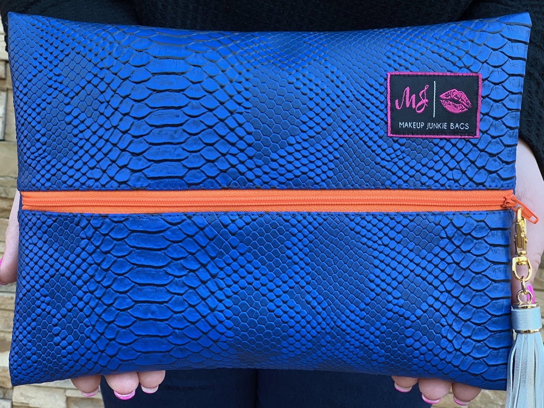 person holding up a Makeup Junkie bag with cobalt blue snakeskin and a bright orange zipper