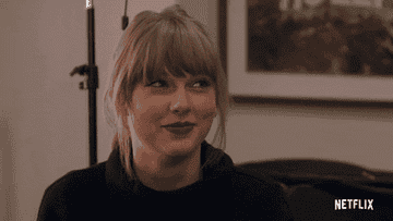 taylor swift in a black turtleneck scrunches her nose