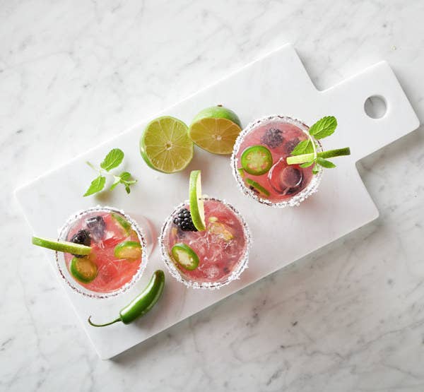 Glasses of Jalapeño and Blackberry Cocktails served on a tray surrounded by cut limes.