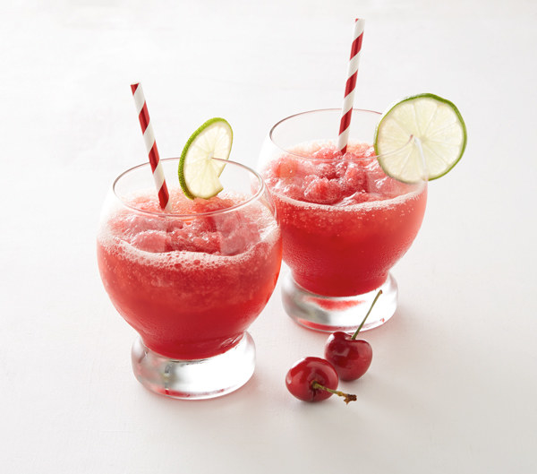 Two round glasses filled with Cherry Lime Vodka Slush, served with lime slices and straws.