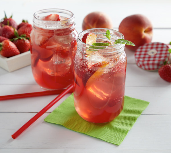 Mason jars filled with Strawberry Peach Tea Cocktail with strawberries and peaches in the background.