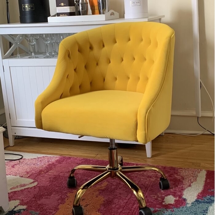 The chair, which has a wingback shape with a raised back and sloping arms, on a gold-toned swivel base