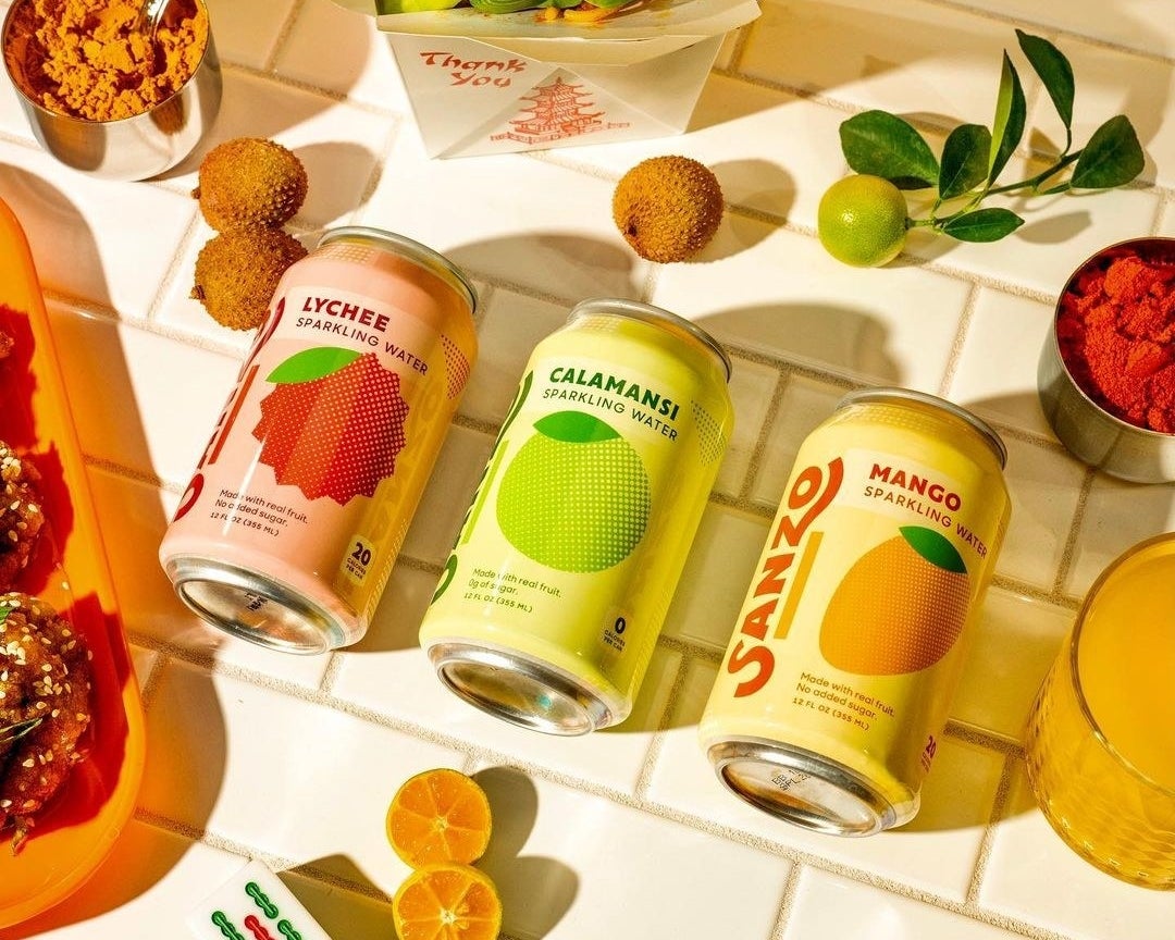 Three different-color cans surrounded by various spices, fruits, and vegetables sitting on a counter 