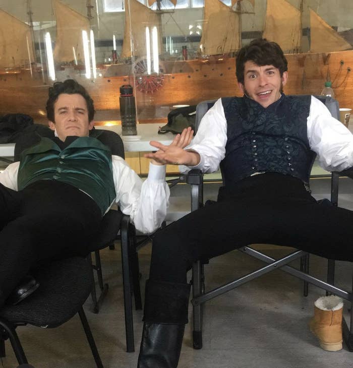 Luke Newton and Jonathan Bailey reclining on chairs on the set of Bridgerton