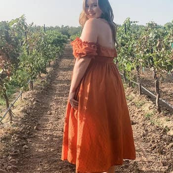 A reviewer wearing the dress in orange in an orchard 
