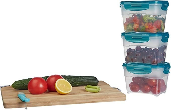 Three containers filled with fruits and veggies, stacked on top of each other. They&#x27;re placed near a chopping board that has veggies and a knife on it.