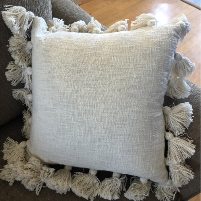 The pillow, which has bunched tassels around the edge, in white