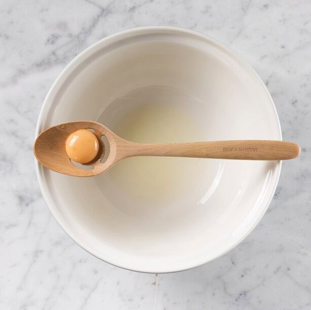 The spoon resting on top of a bowl with an egg yolk in it