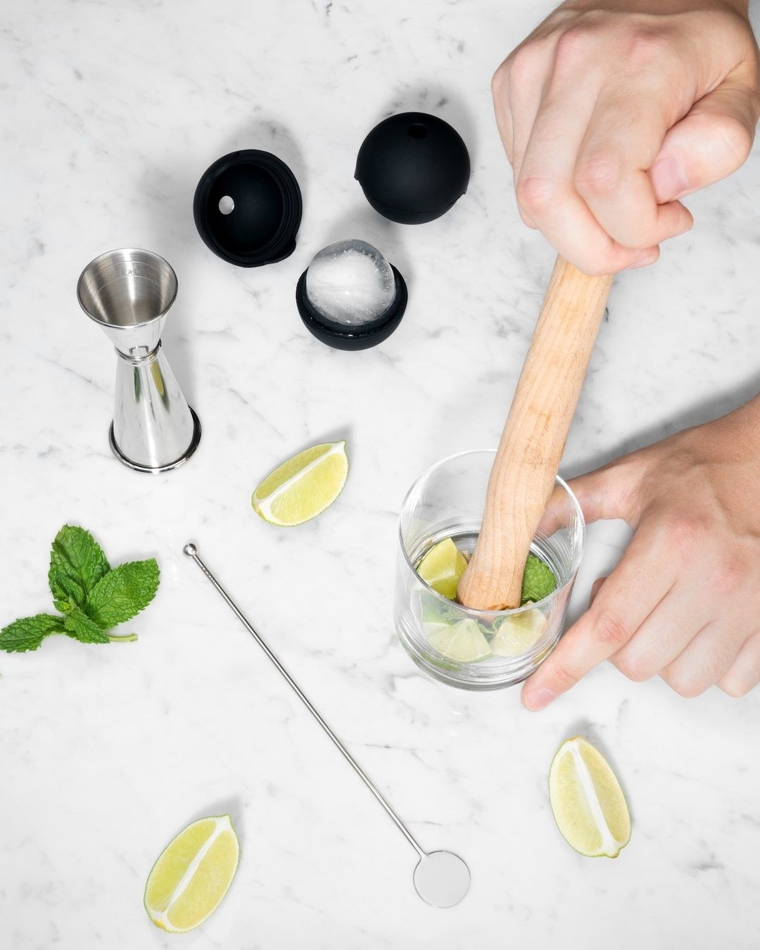 A person using the kit to muddle limes and mint for a cocktail