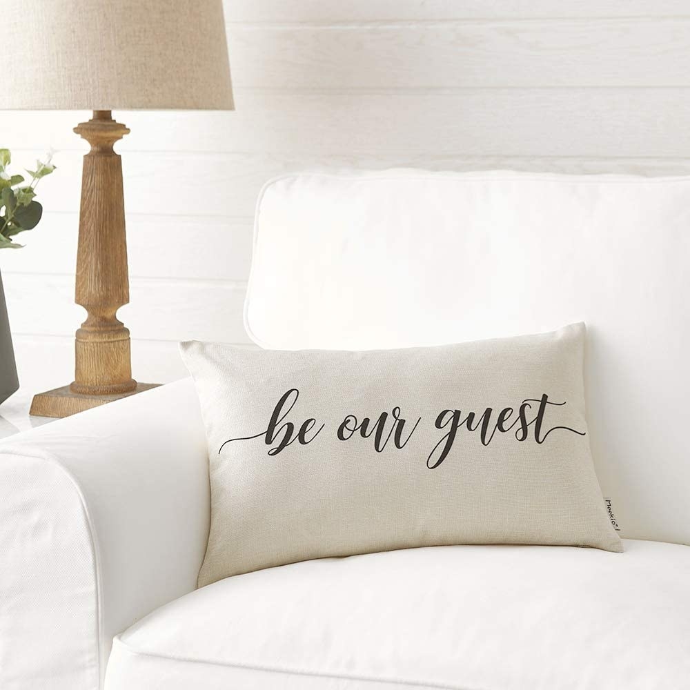 Small rectangular ivory pillow with &quot;be our guest&quot; written in black cursive 