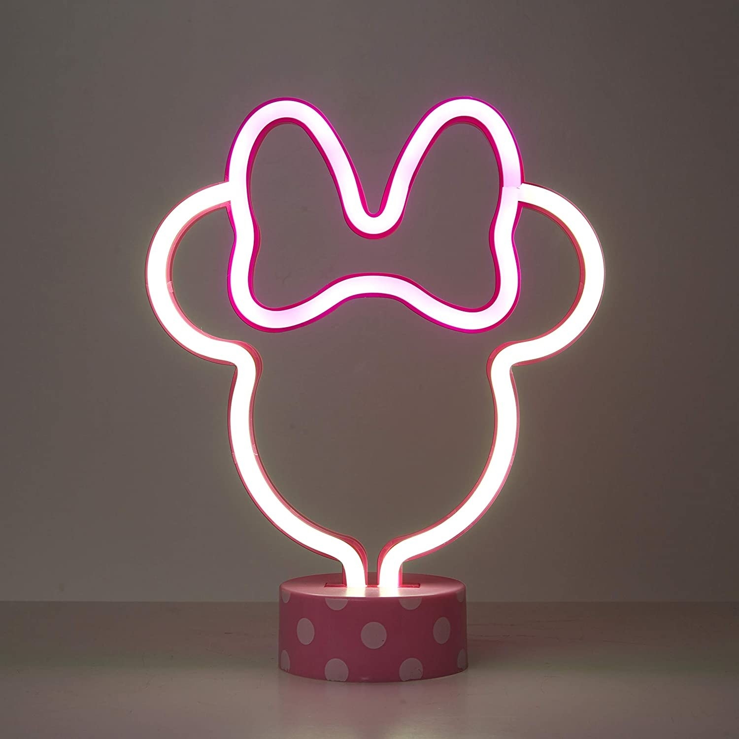 A small Minnie Mouse shaped minimalist neon lamp with a pink and white polka dot base 
