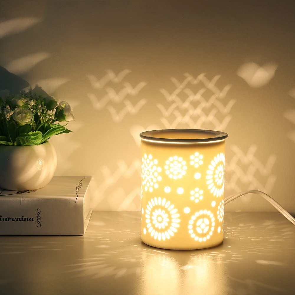 A yellow wax warmer with flower cutouts lit up to reflect patterns on the wall 
