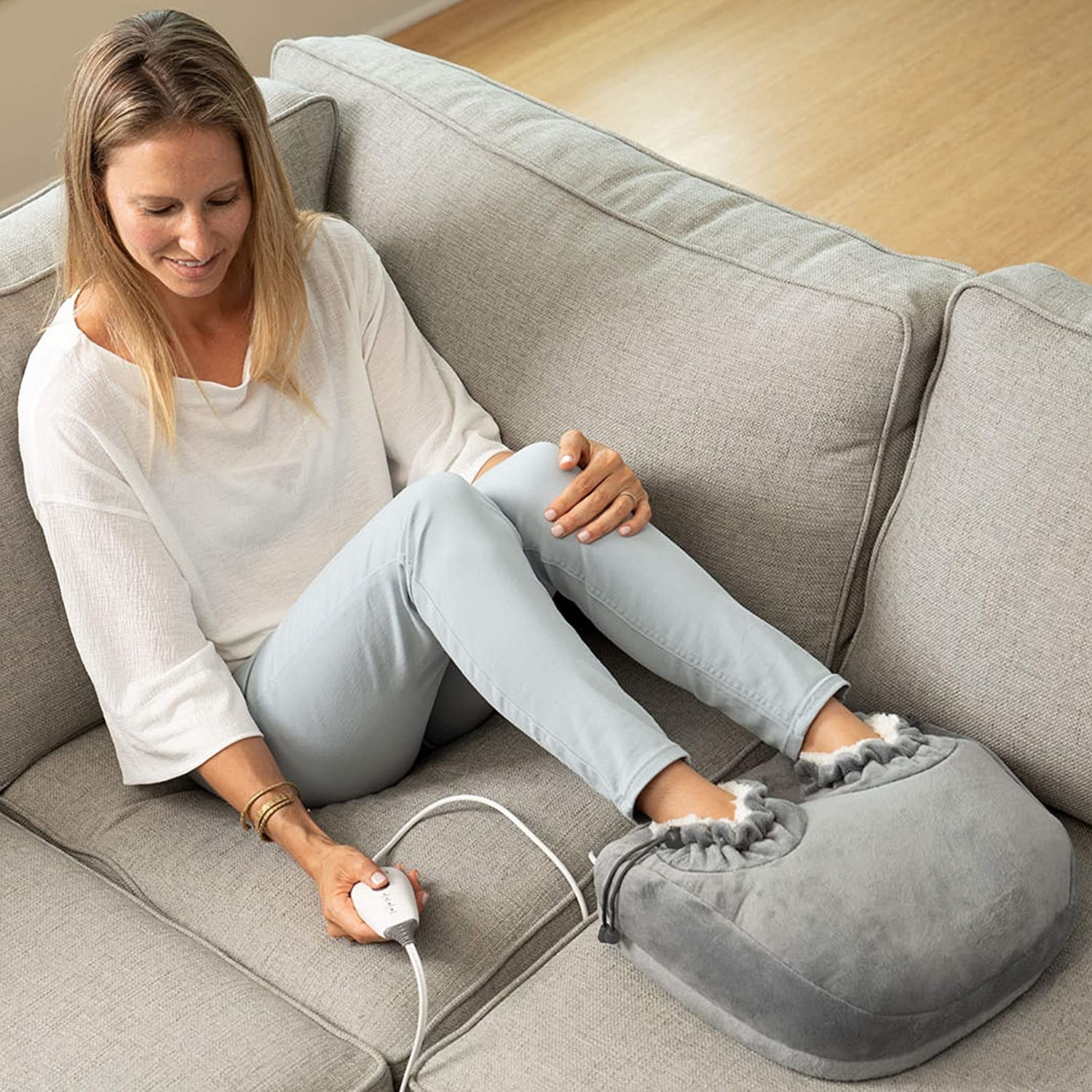 Person on sofa with feet inside large plush foot heater, with one hole per foot and cinches to make it extra secure