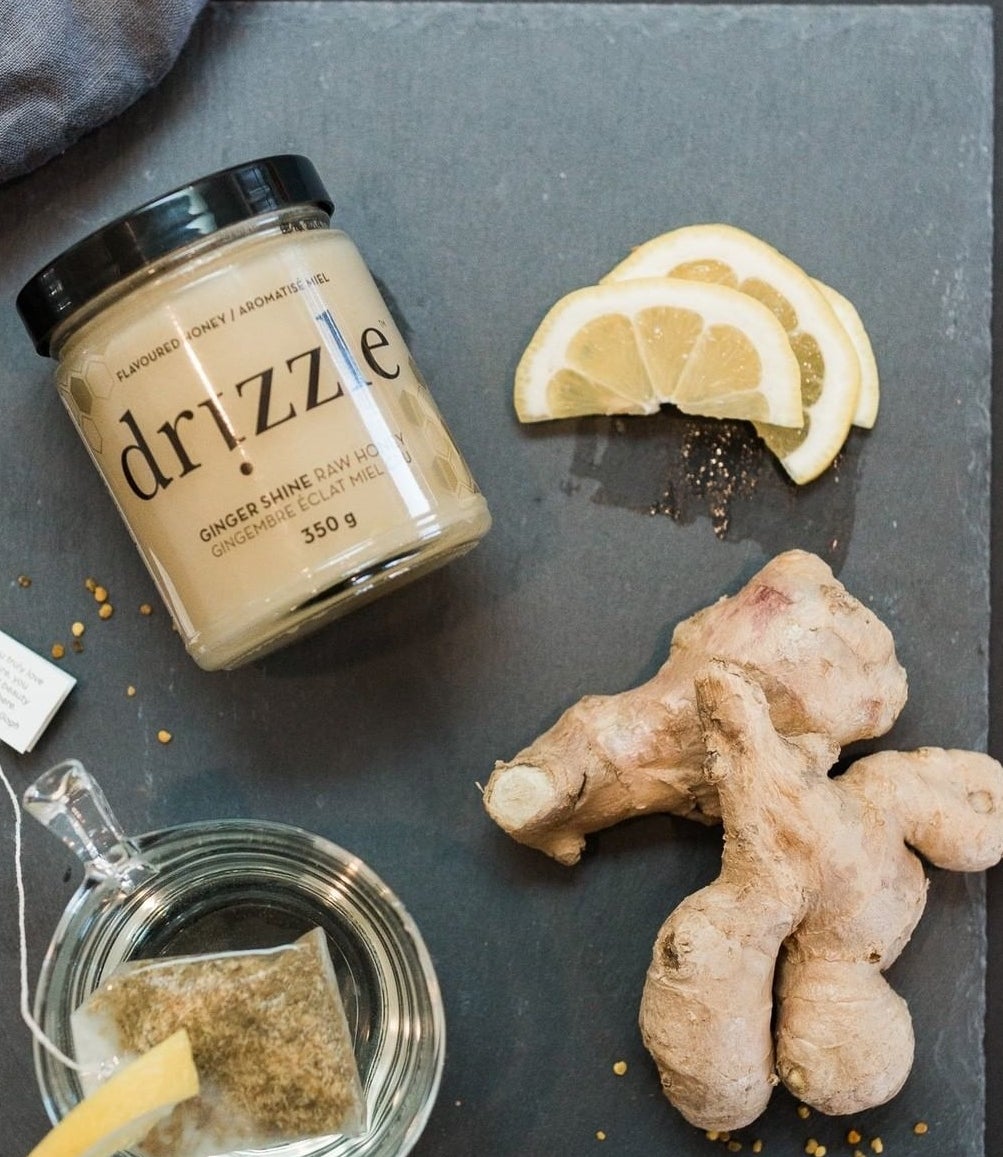 A flatlay of a jar of the infused honey next to fresh ginger root, lemon slices, and a mug of tea