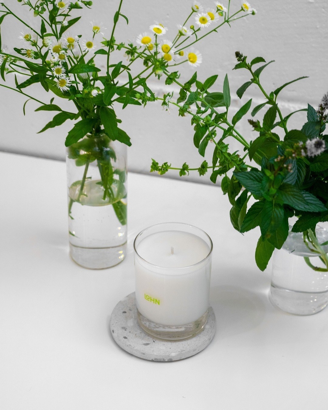 A scented candle next to a vase full of various herbs