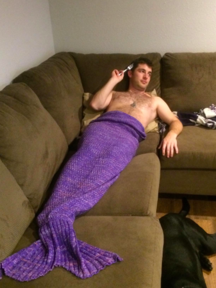 a reviewer wearing the purple mermaid tail blanket on a couch with a fork in their hair
