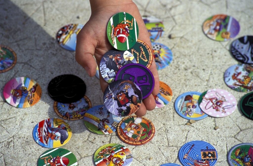 Kids hand holding pogs with more pogs on the ground