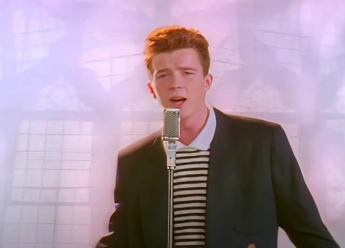 Screen shot of Rick Astley singing into a microphone in his music video for &quot;Never Gonna Give It Up&quot;