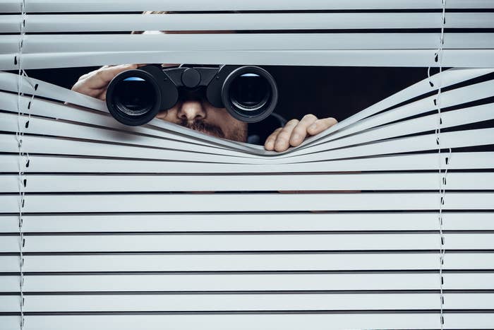 Spy looking with binoculars through blinds