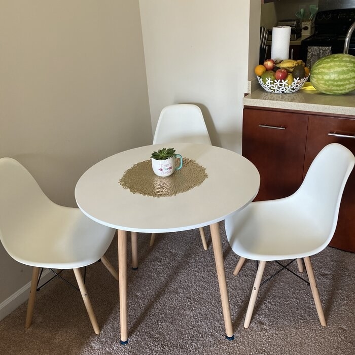 The table, which has a round white top, and splayed wooden legs