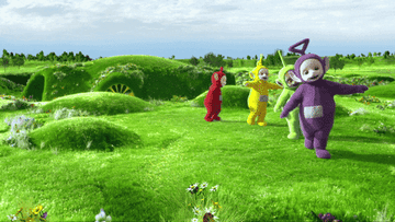 All four Teletubbies running across the grass with their arms outstretched 