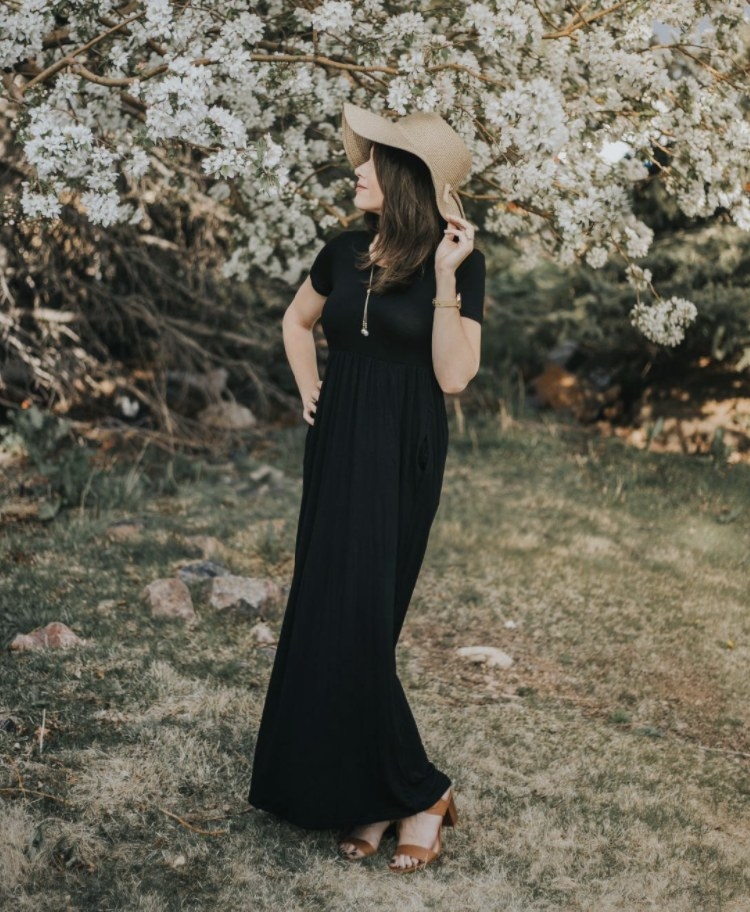 A person is wearing a black maxi dress, sun hat, and camel sandals
