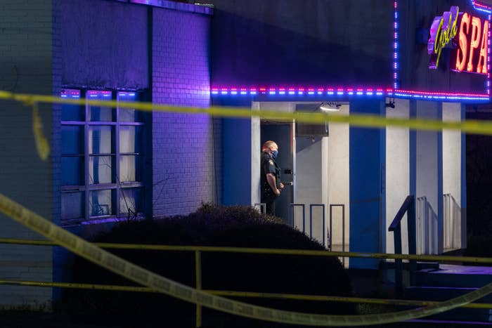 A police officer stands outside the entrance of a spa, where caution tape is hung up