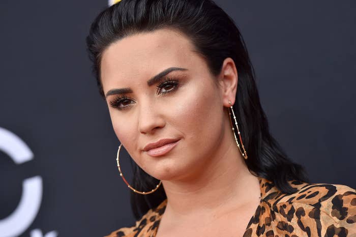 Demi posing on a red carpet in a leopard-print outfit and hoop earrings