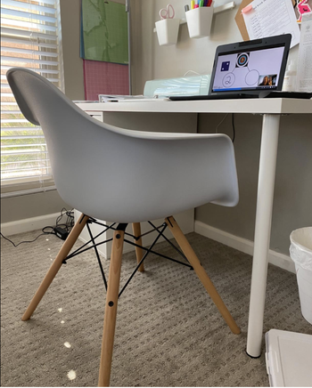 White office chair with four light brown legs in front of desk 
