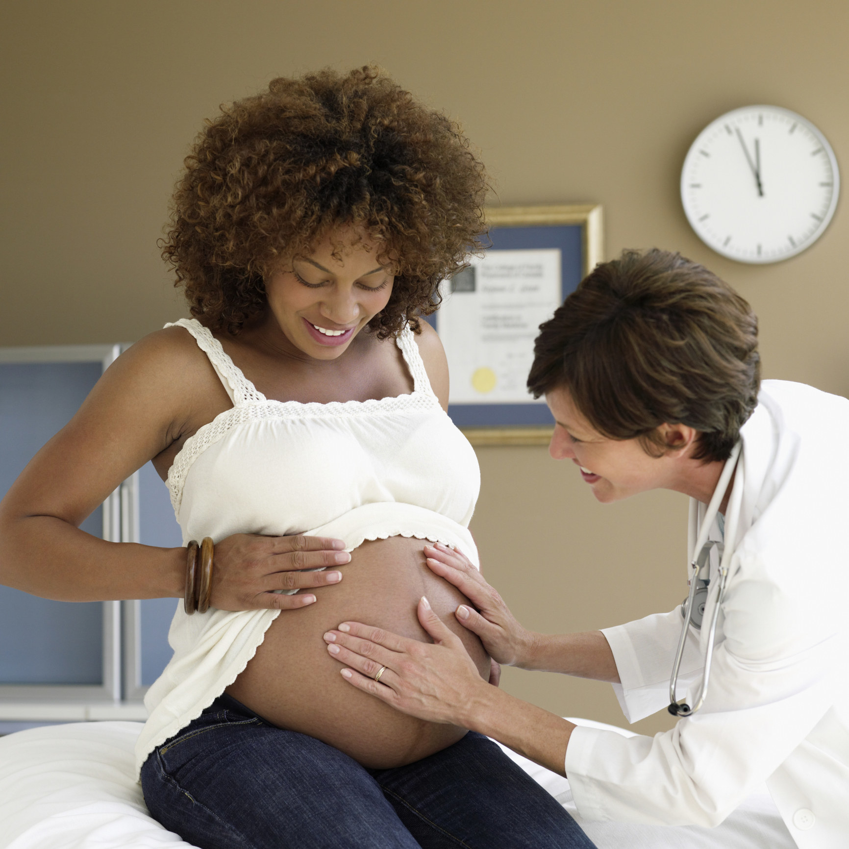 A white doctor touching the belly of a Black pregnant woman