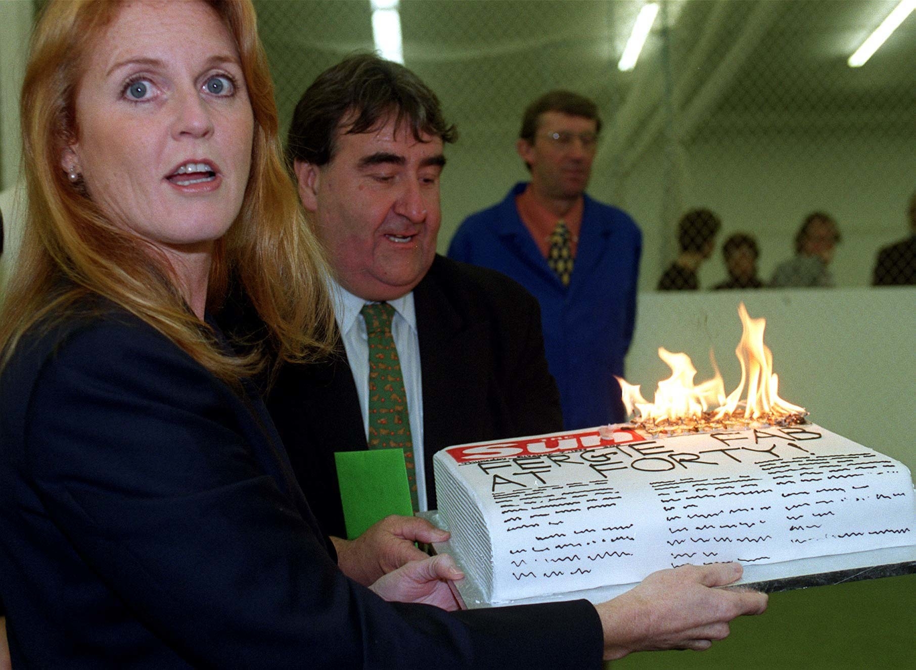 Duchess of York holding a cake shaped like a newspaper that&#x27;s on fire