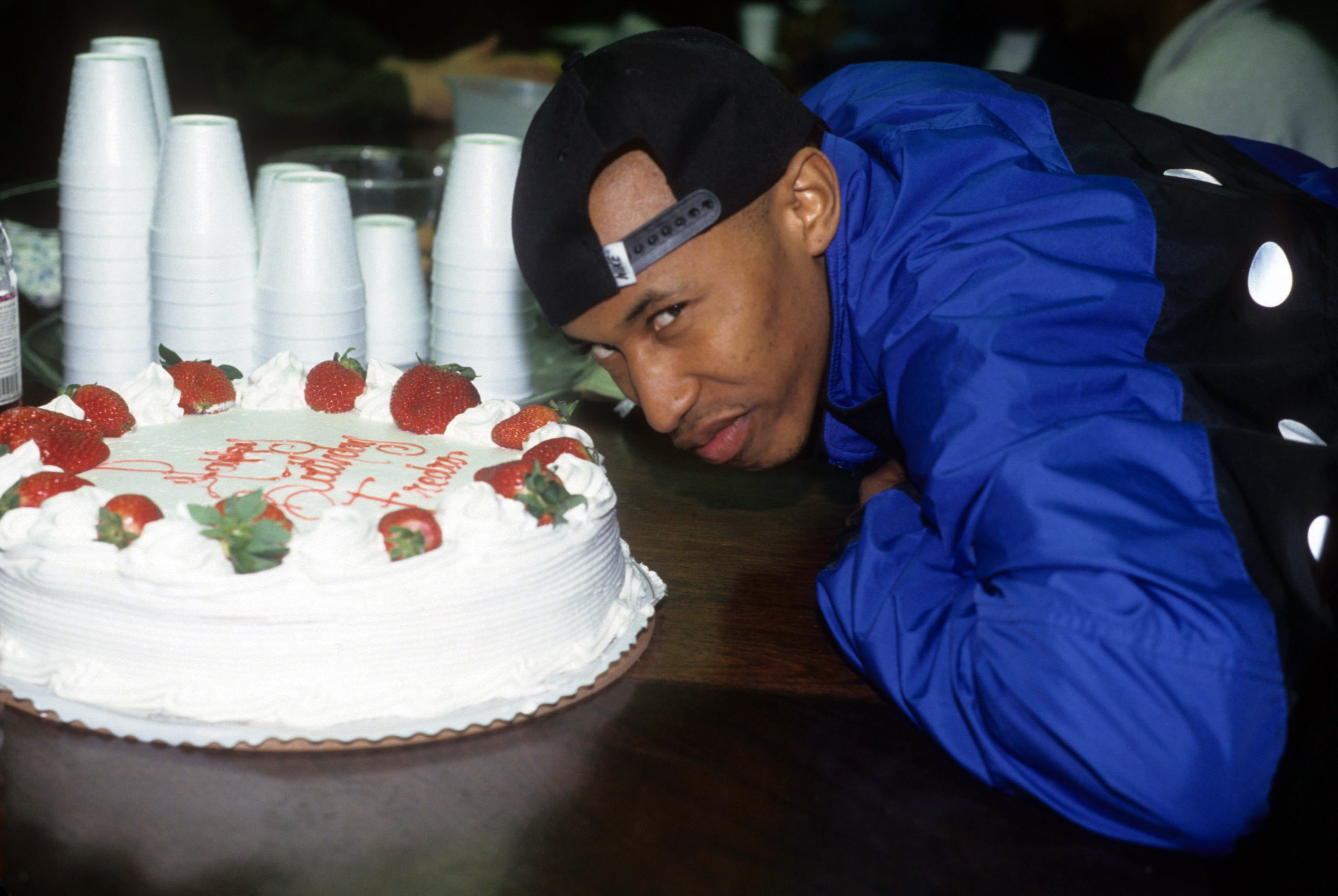 Fredo Starr in a blue jacket in front of a cake with strawberries and writing 