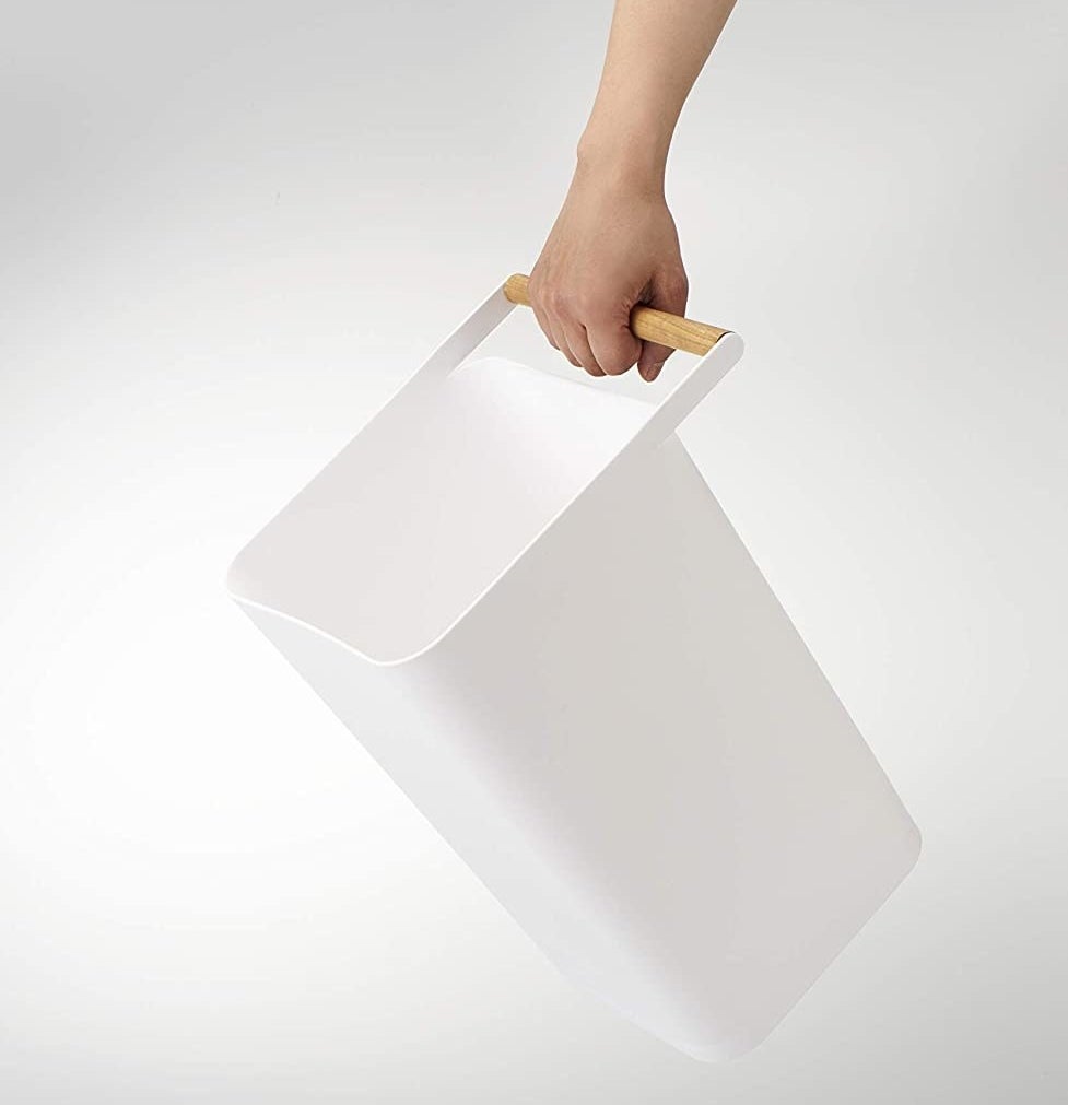 A white square shaped trashcan with a wooden handle on the lid 