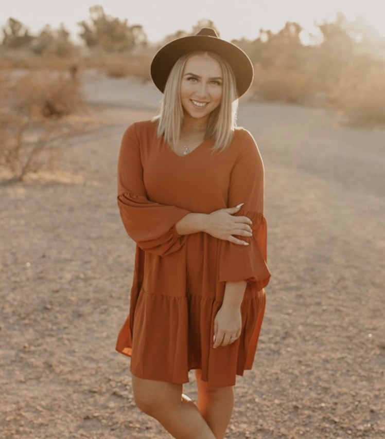 A person wearing a burnt orange shift dress and a black hat