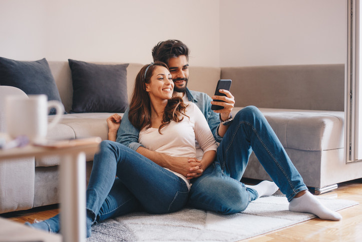 Couple sitting on the living room floor and looking at a phone while smiling